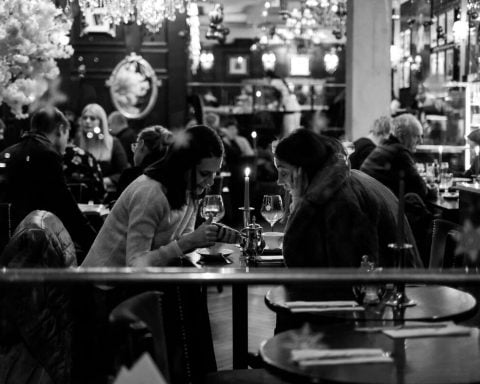 dwie kobiety siedzące przy stoliku w restauracji, pijące wino
