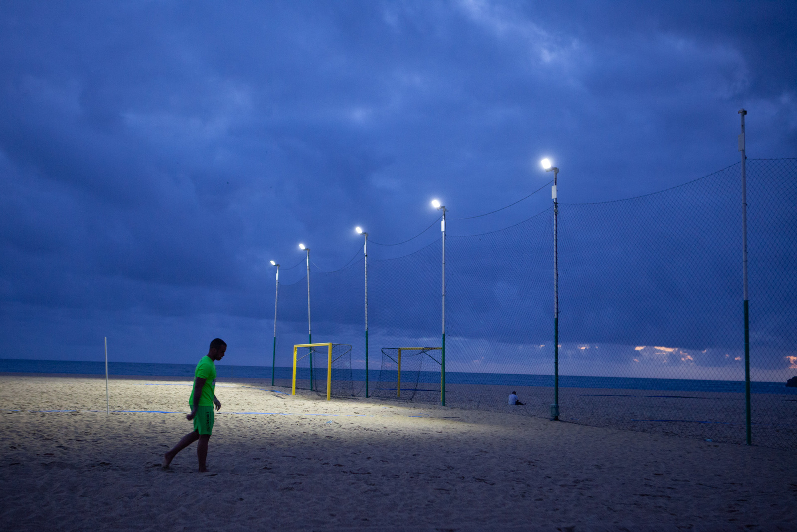Nazaré, Portugalia. Mężczyzna w sportowym stroju idzie obok boiska na plaży w świetle nadchodzącego zmierzchu