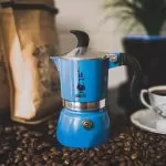kawiarka moka stojąca na stole pośród ziaren kawy