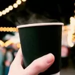 kubek z kawą trzymany w dłoni na tle świątecznych dekoracji, jarmark bożonarodzeniowy