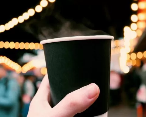 kubek z kawą trzymany w dłoni na tle świątecznych dekoracji, jarmark bożonarodzeniowy