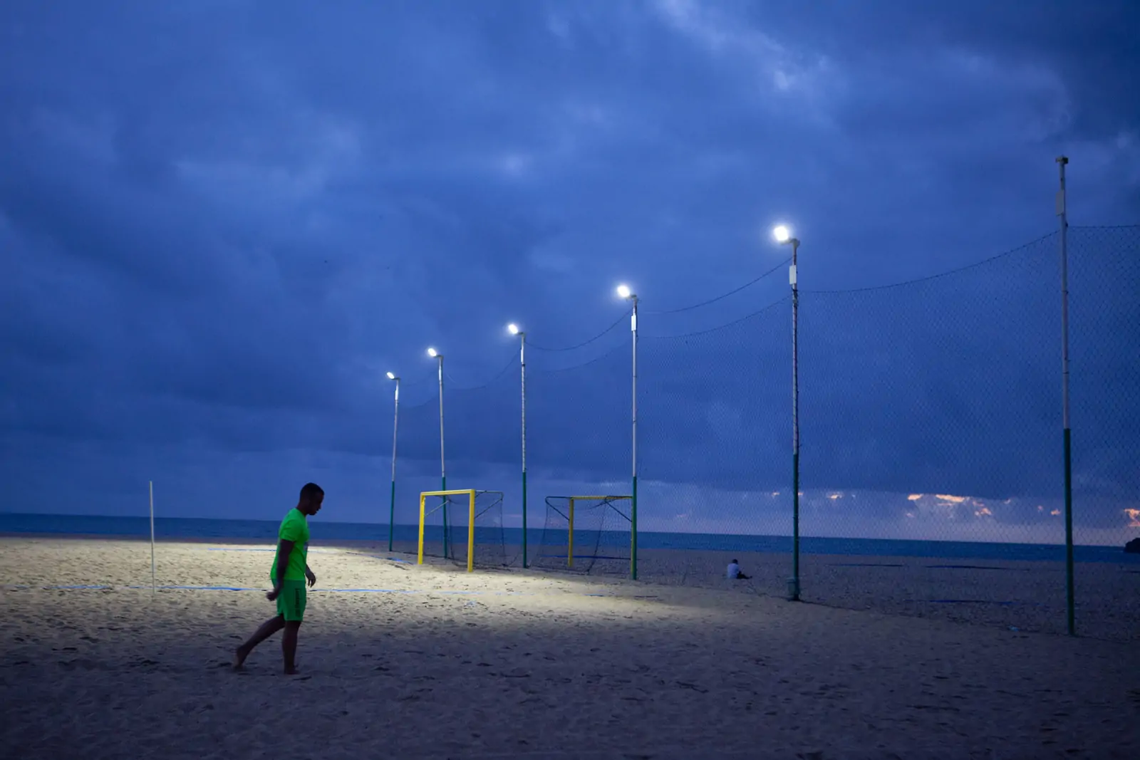 Nazaré, Portugalia. Mężczyzna w sportowym stroju idzie obok boiska na plaży w świetle nadchodzącego zmierzchu